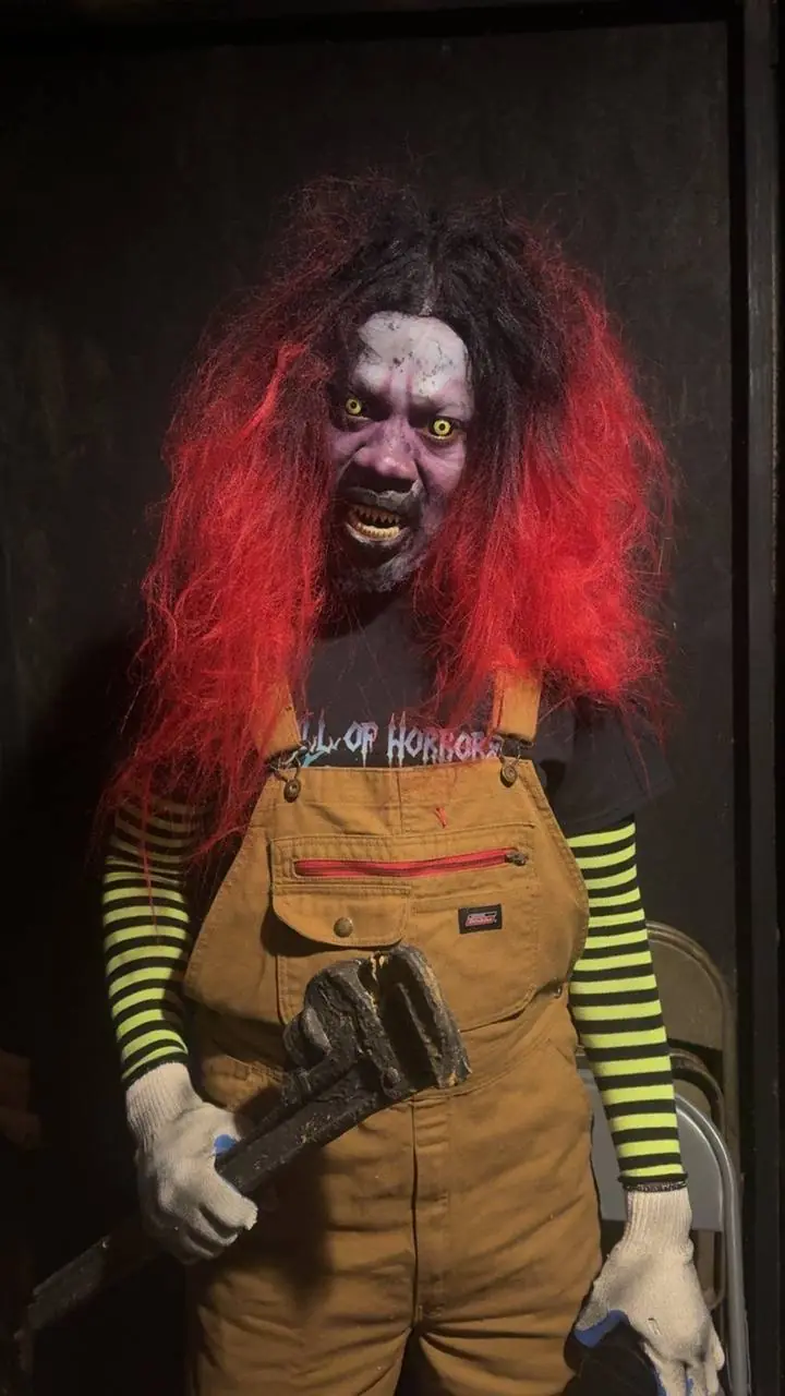 A Hall of Horrors actor in full monster makeup, red hair, yellow eyes and a pipe wrench